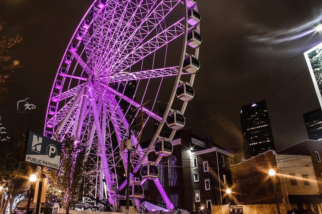 Ferris wheel glowing purple over a downtown street at night