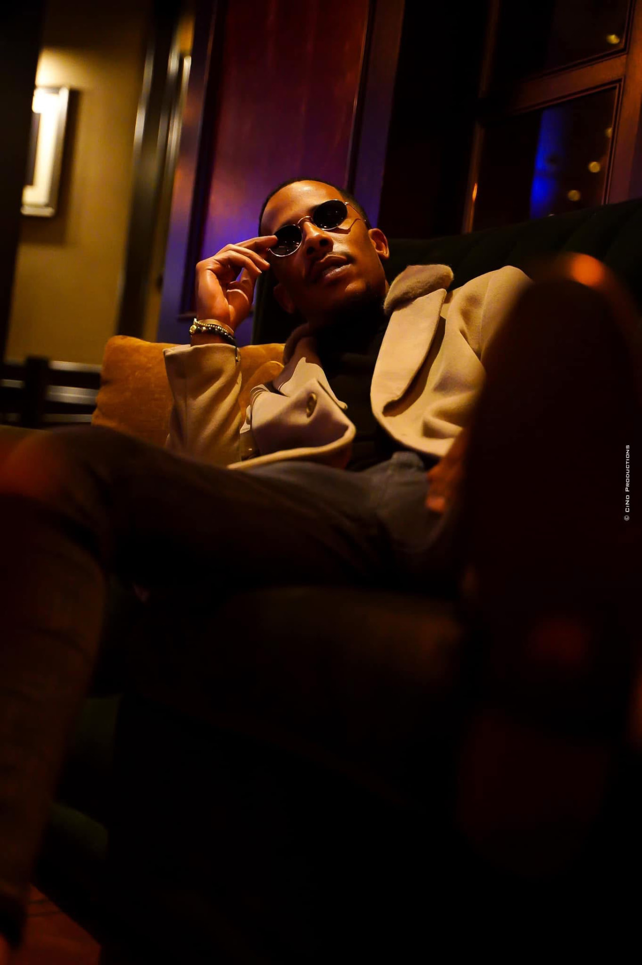 Moody lounge portrait of a man in sunglasses under warm light