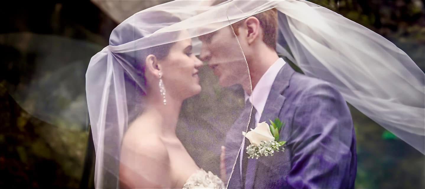 Couple face to face beneath a flowing veil