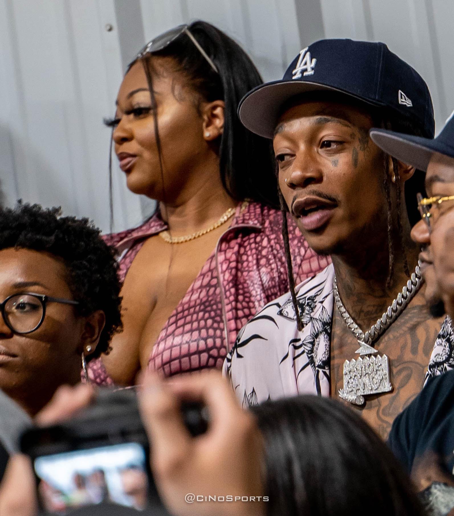 Artist in an LA cap surrounded by crowd and cameras at a live event