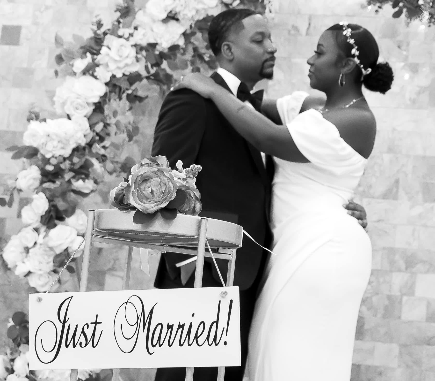 Newlyweds embracing behind a Just Married sign and floral arch