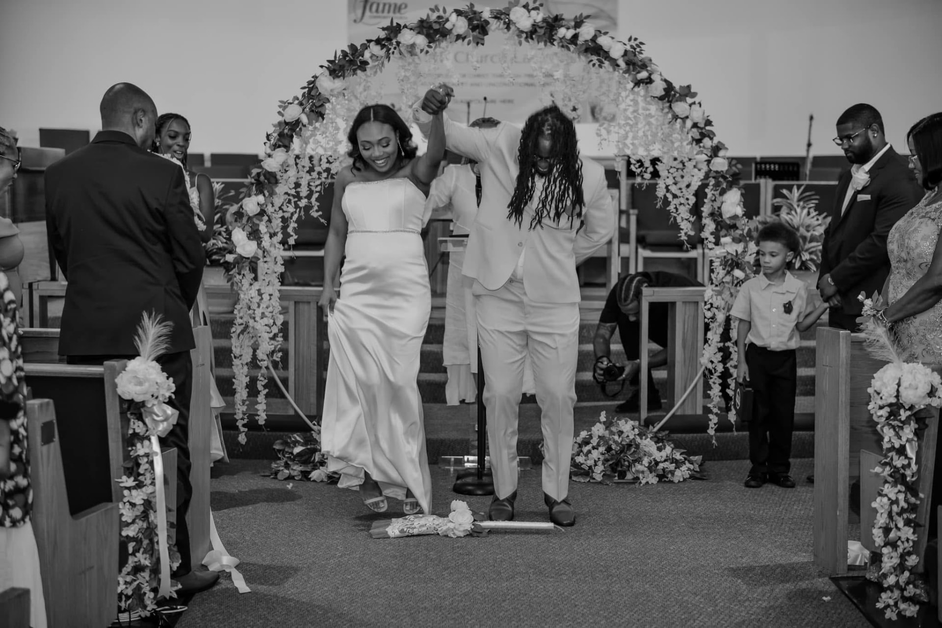 Couple jumping the broom as guests cheer in the church aisle