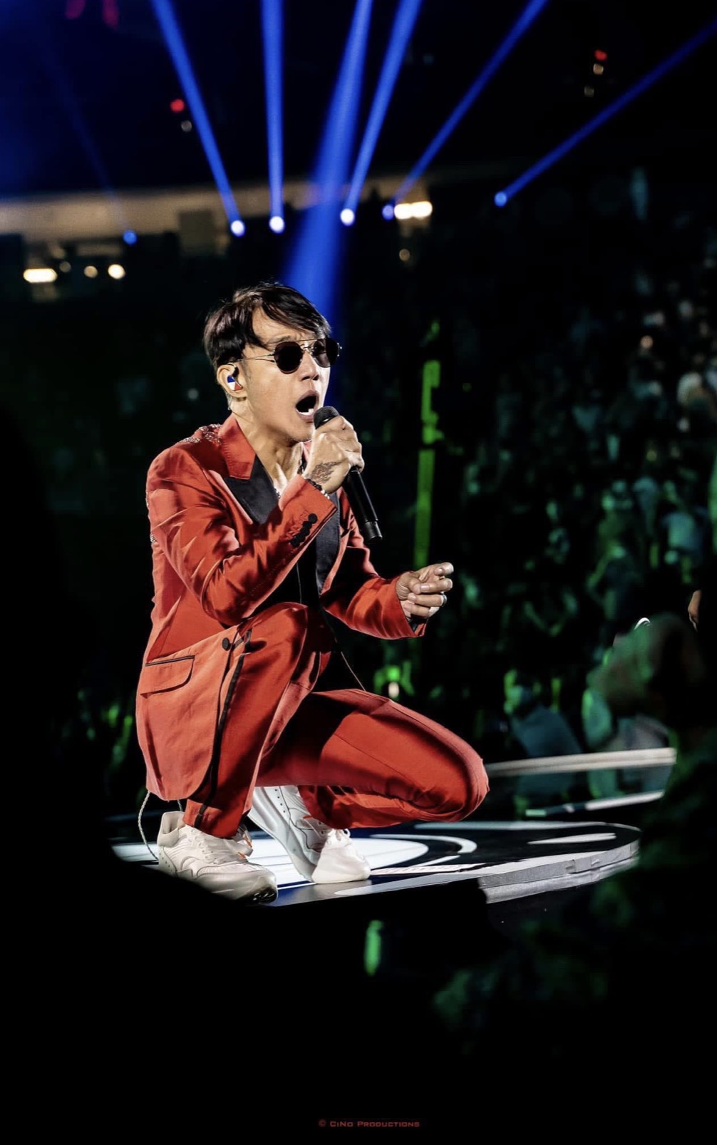 Performer in a red suit kneeling on an arena stage mid-song