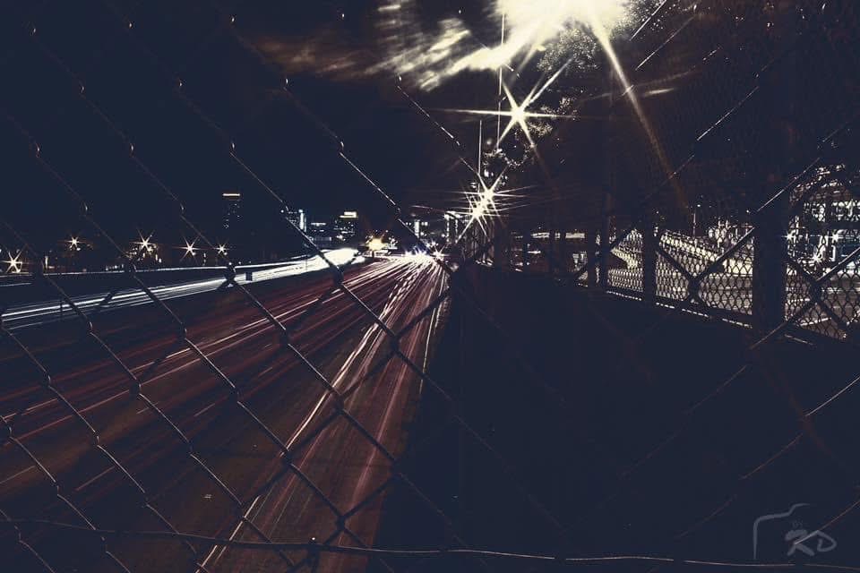 Long-exposure highway light trails seen through a chain link fence